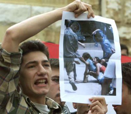 A Lebanese student, during a sit-in, holds a picture of his brutalized  colleagues in a  previous demonstration against Syrian occupation 